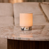Dou Small cordless table lamp in white marble glowing on a coffee table beside a beige sofa