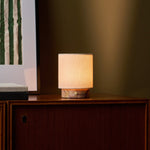 Oplaadbare tafellamp Dou Small verlicht op een notenhouten dressoir naast een groen gestreepte botanische print