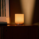 Tafellamp oplaadbaar Dou Small brandt warm op een donkere houten console naast gestreepte wandkunst