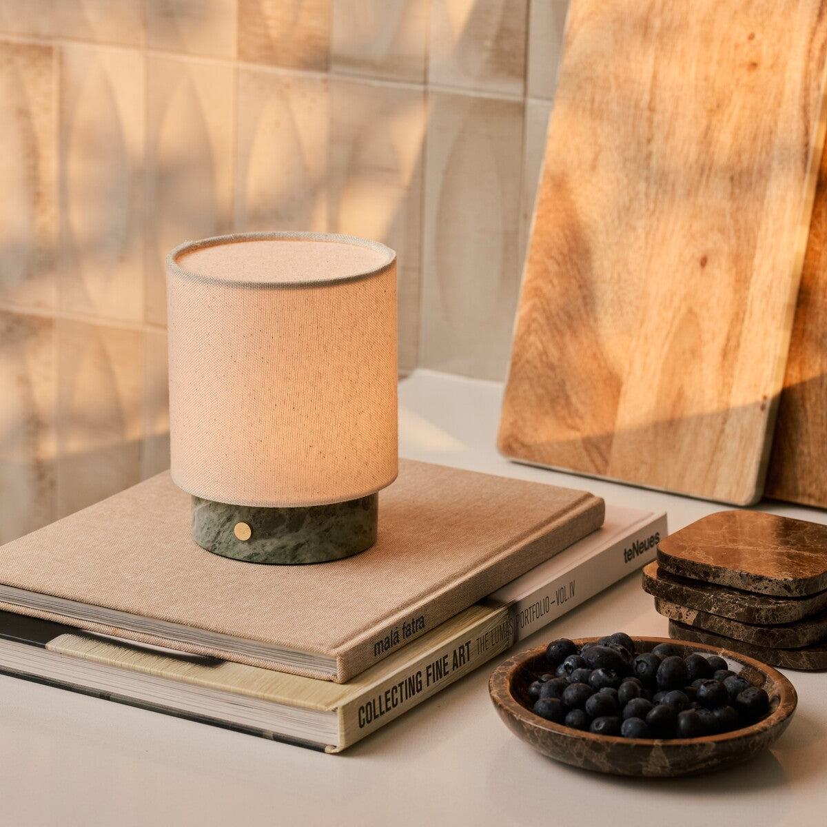 Cordless table lamp Dou Small, Ice Green marble, styled on stacked books beside blueberries and wood boards