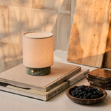 Cordless table lamp Dou Small, Ice Green marble, styled on stacked books beside blueberries and wood boards