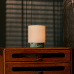 Cordless table lamp Dou Small in Ice Green marble casting warm light through striped blind shadows