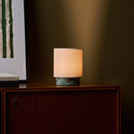 Dou Small rechargeable table lamp in Ice Green marble glowing on a wood sideboard at night