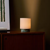 Dou Small rechargeable table lamp in Ice Green marble glowing on a wood sideboard at night