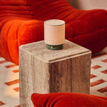Cordless table lamp Dou Small, Ice Green marble, styled on a travertine side table beside a red sofa