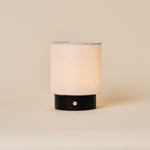 Rechargeable table lamp Dou Small in Nero Marquina black marble with a natural linen drum shade on a plain beige backdrop