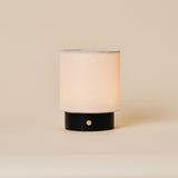 Rechargeable table lamp Dou Small in Nero Marquina black marble with a natural linen drum shade on a plain beige backdrop