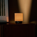 Tavellio Dou Small rechargeable table lamp in Nero Marquina marble glowing warmly on a dark wood cabinet