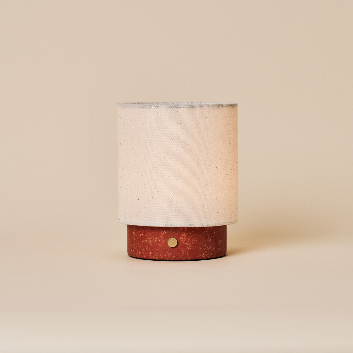 Dou Small cordless table lamp in red travertine with linen shade on a plain cream backdrop