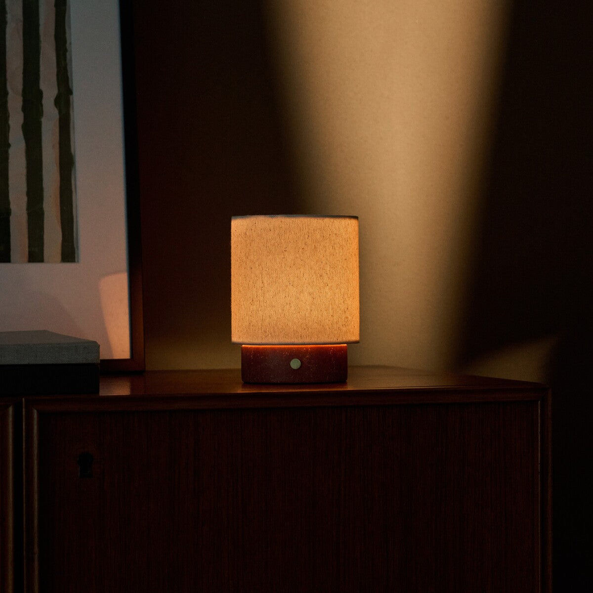Dou Small cordless table lamp in red travertine on a wood cabinet with striped artwork close-up