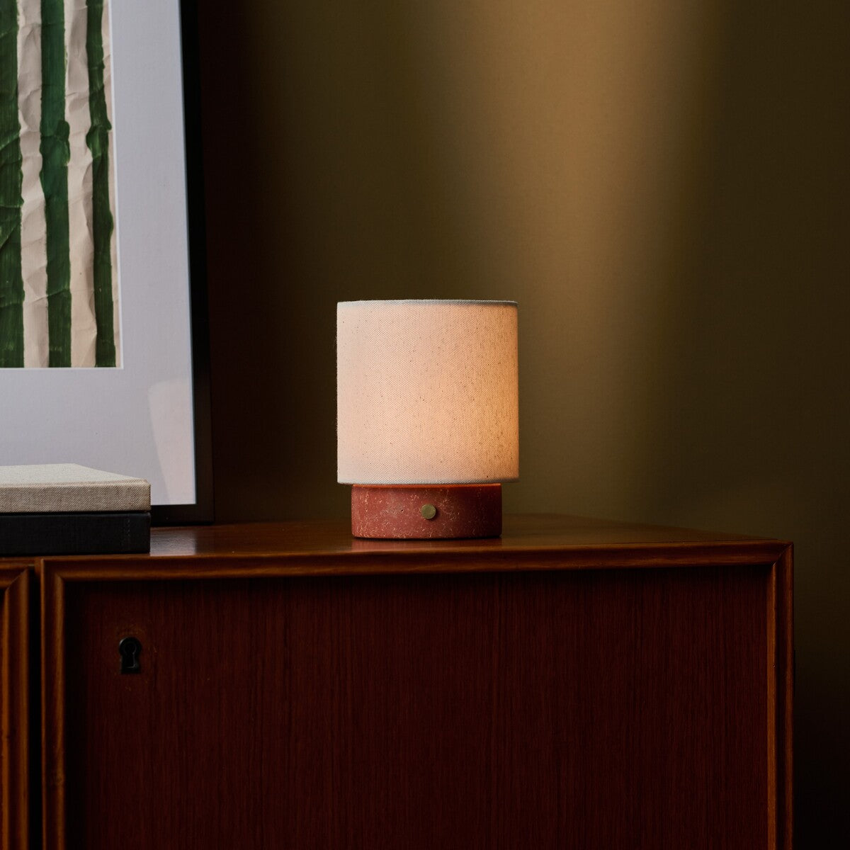 Dou Small rechargeable table lamp in red travertine glowing on a walnut sideboard beside framed art