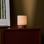 Dou Small rechargeable table lamp in red travertine glowing on a walnut sideboard beside framed art