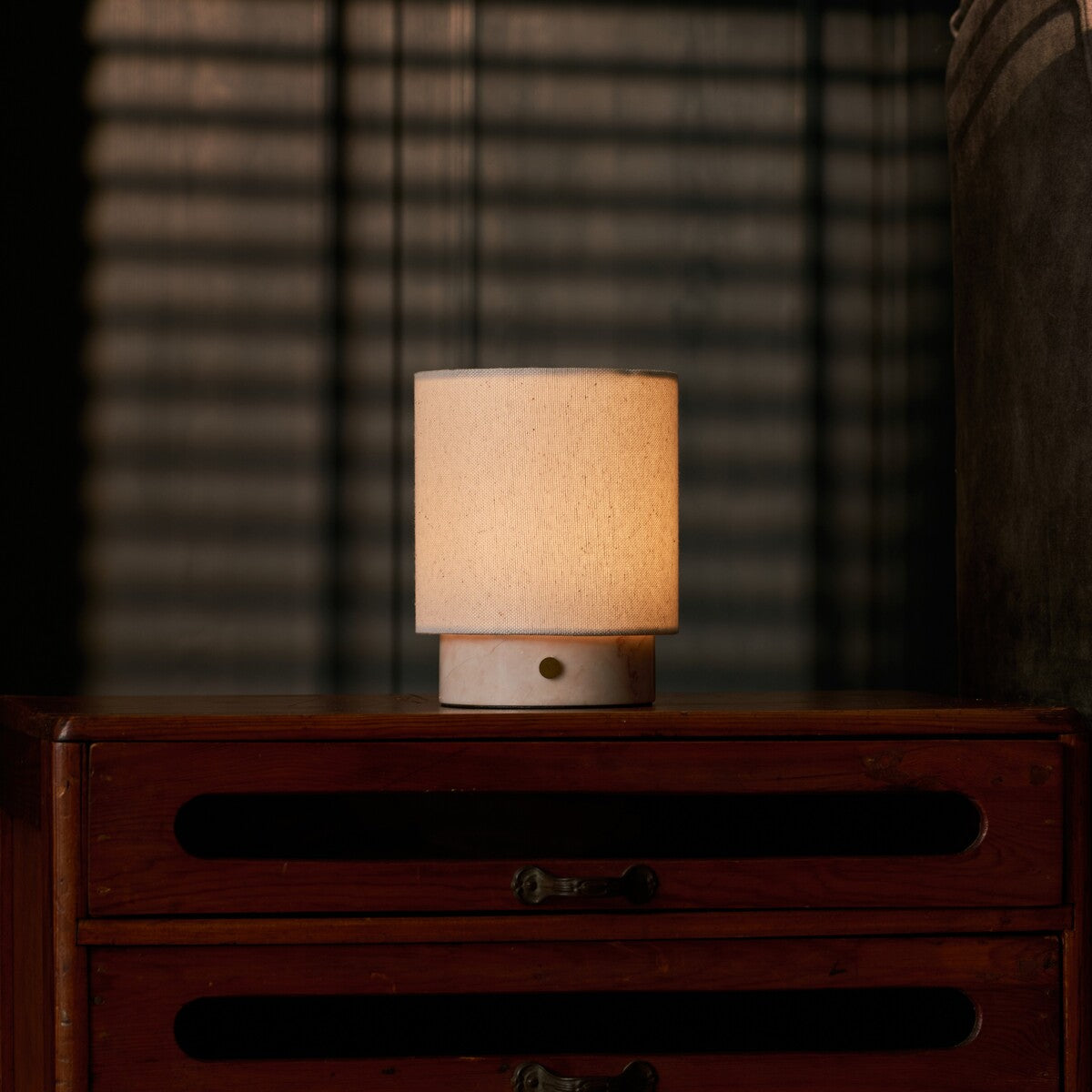 Dou Small rechargeable table lamp in Rosa Aurora marble on a vintage dresser with blind-shadow light
