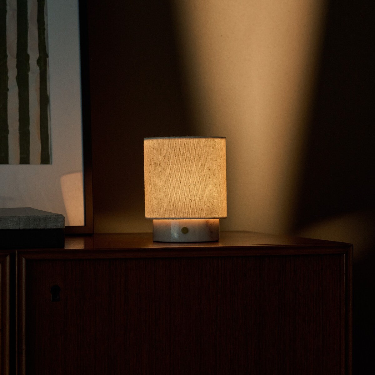 Dou Small rechargeable table lamp in Rosa Aurora marble glowing softly on a dark wood cabinet