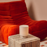 Dou Small cordless table lamp in Rosa Aurora marble glowing on a travertine table, red chair in the background