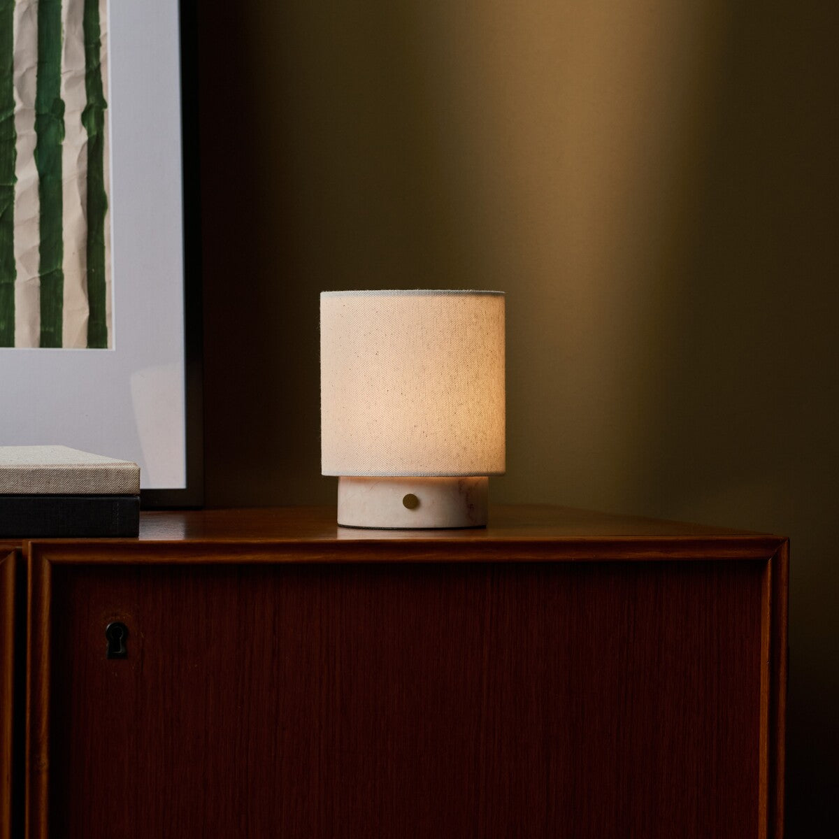 Dou Small cordless table lamp in Rosa Aurora marble beside striped wall art on a walnut sideboard
