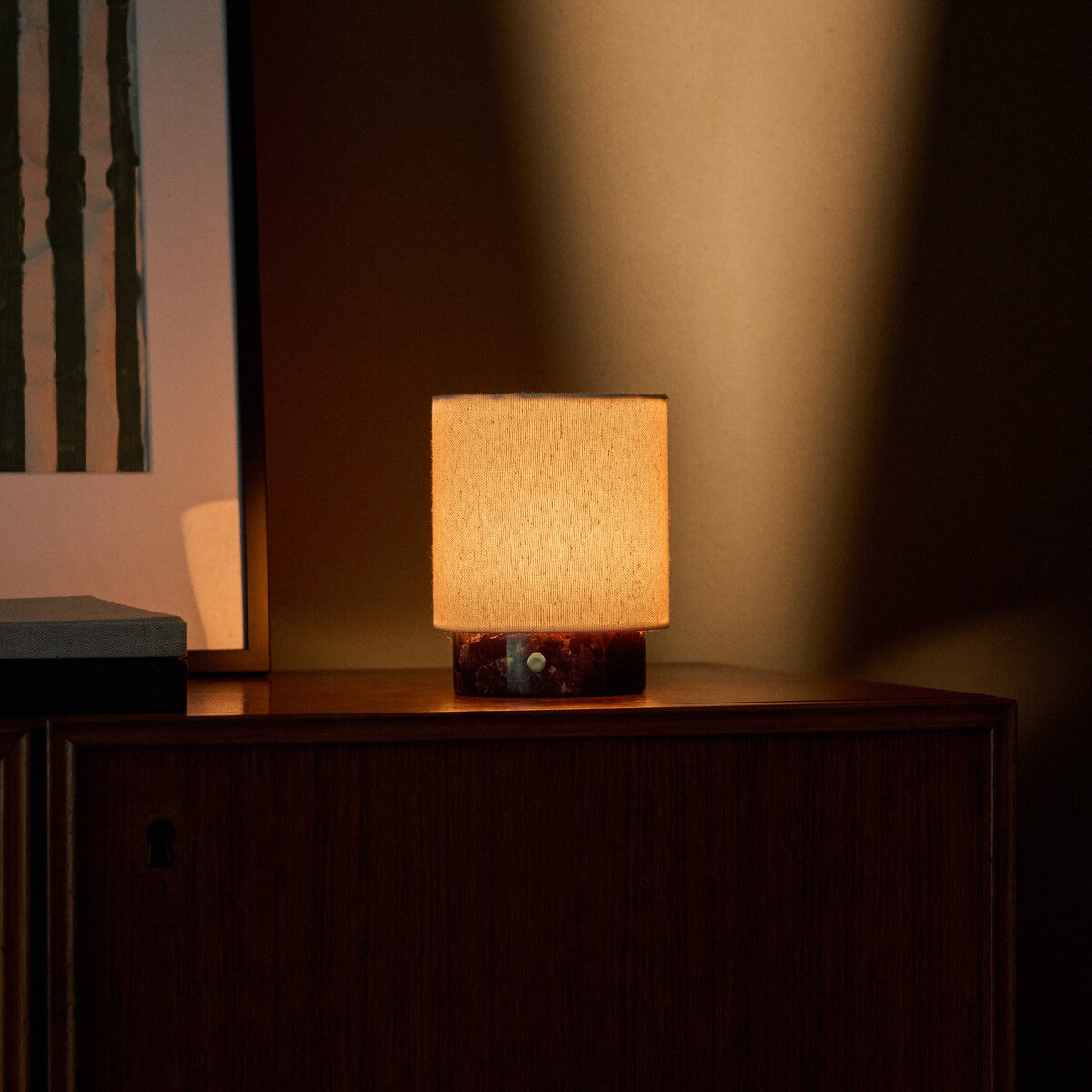 Rechargeable table lamp Dou Small in Rosso Levanto marble glowing softly against a dark cabinet interior