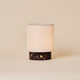 Rechargeable table lamp Dou Small in Rosso Levanto red marble with a natural linen shade on a beige backdrop
