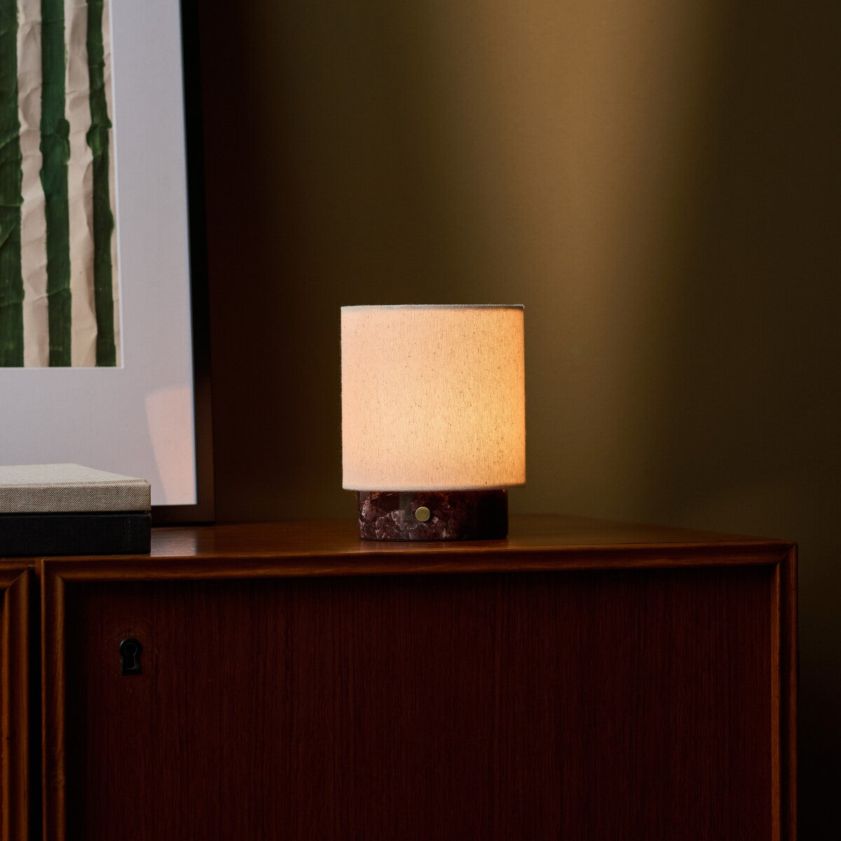 Tavellio Dou Small cordless table lamp in Rosso Levanto marble casting warm light on a wooden cabinet