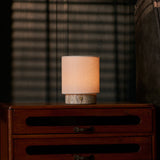 Cordless Dou Small Silver Travertine Table Lamp glowing on a dresser beside a grey upholstered armchair