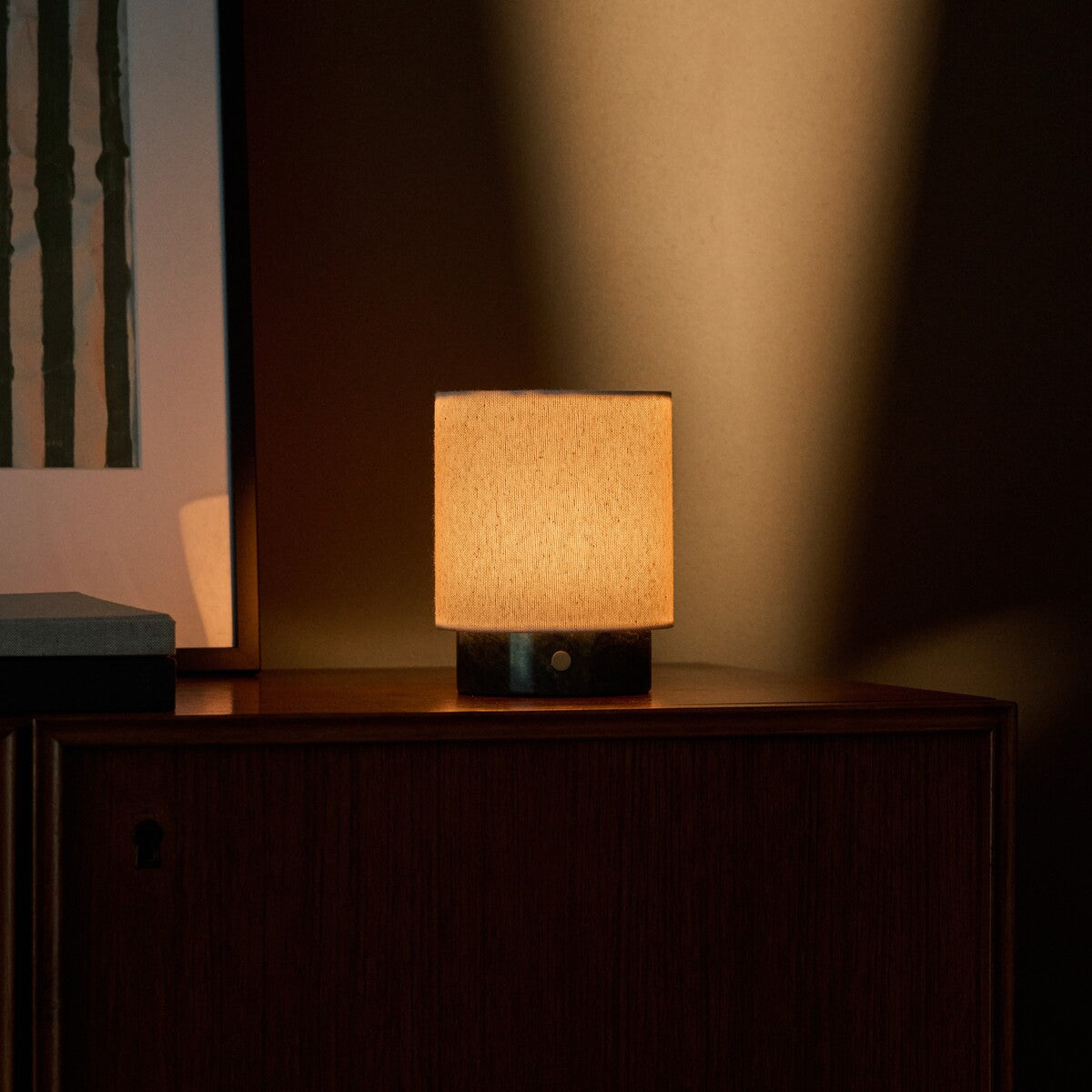 Rechargeable table lamp Dou Small in Verde Alpi marble casting warm light against a dark cabinet