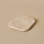 Fi square travertine coaster with natural stone texture on a neutral beige background