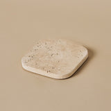 Fi square travertine coaster with natural stone texture on a neutral beige background