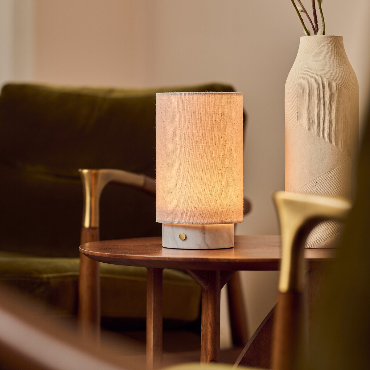Floris cordless table lamp with white marble base glowing on a side table beside a green velvet armchair