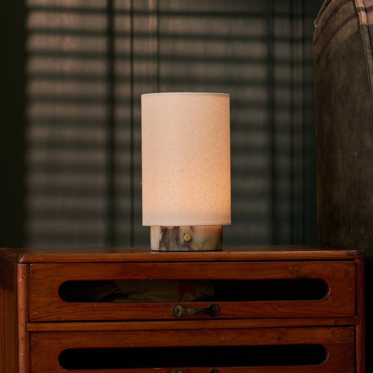 Floris rechargeable table lamp in Calacatta Viola marble glowing on a bedroom dresser before striped blinds