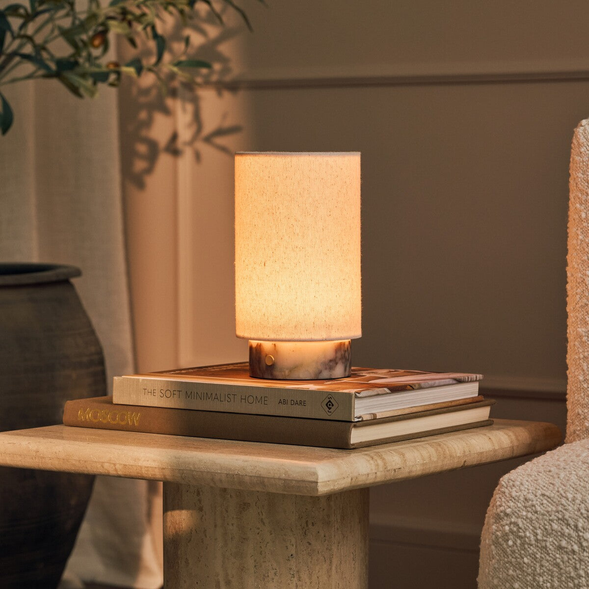 Tavellio Floris cordless table lamp in Calacatta Viola marble glowing atop stacked books on a travertine table
