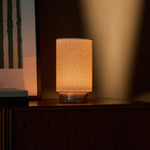Tafellamp oplaadbaar Floris in roze marmer, warm gloeiend op een houten dressoir in de schemering