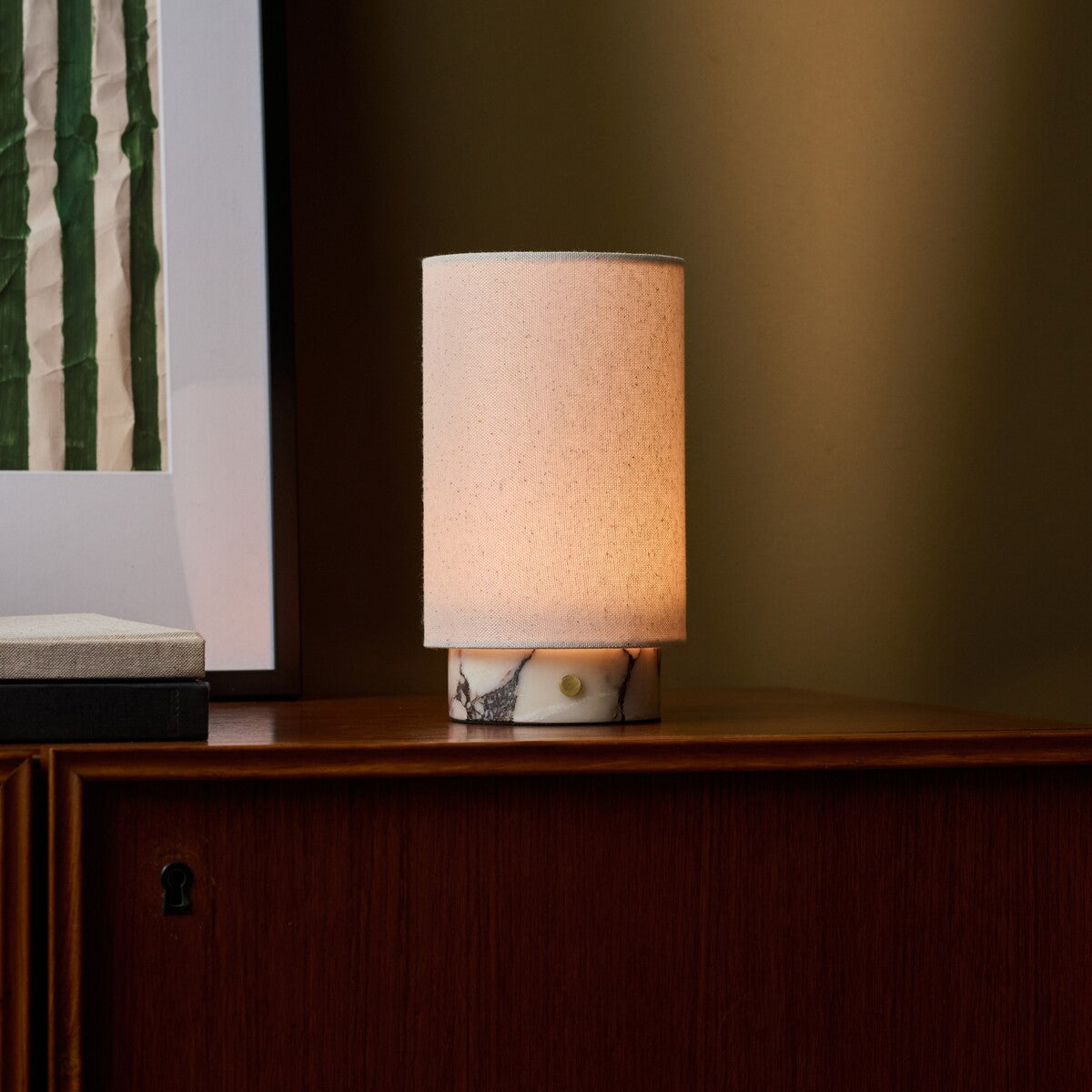 Floris rechargeable table lamp in Calacatta Vionaro white marble lit on a wooden sideboard beside framed art