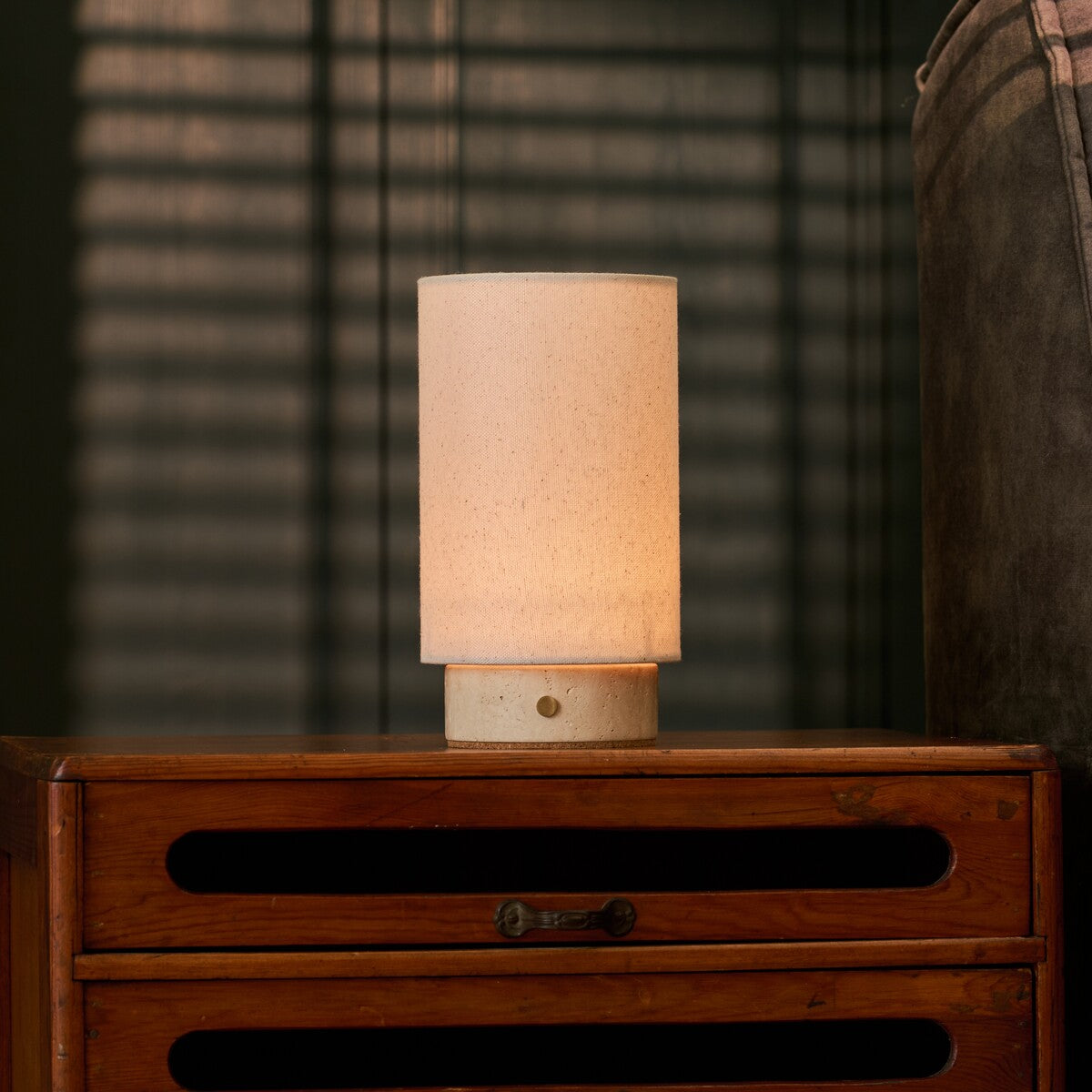 Floris rechargeable table lamp with travertine base on a bedroom dresser beside striped window blinds