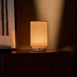 Floris rechargeable table lamp with travertine base glowing on a cabinet corner against an olive wall