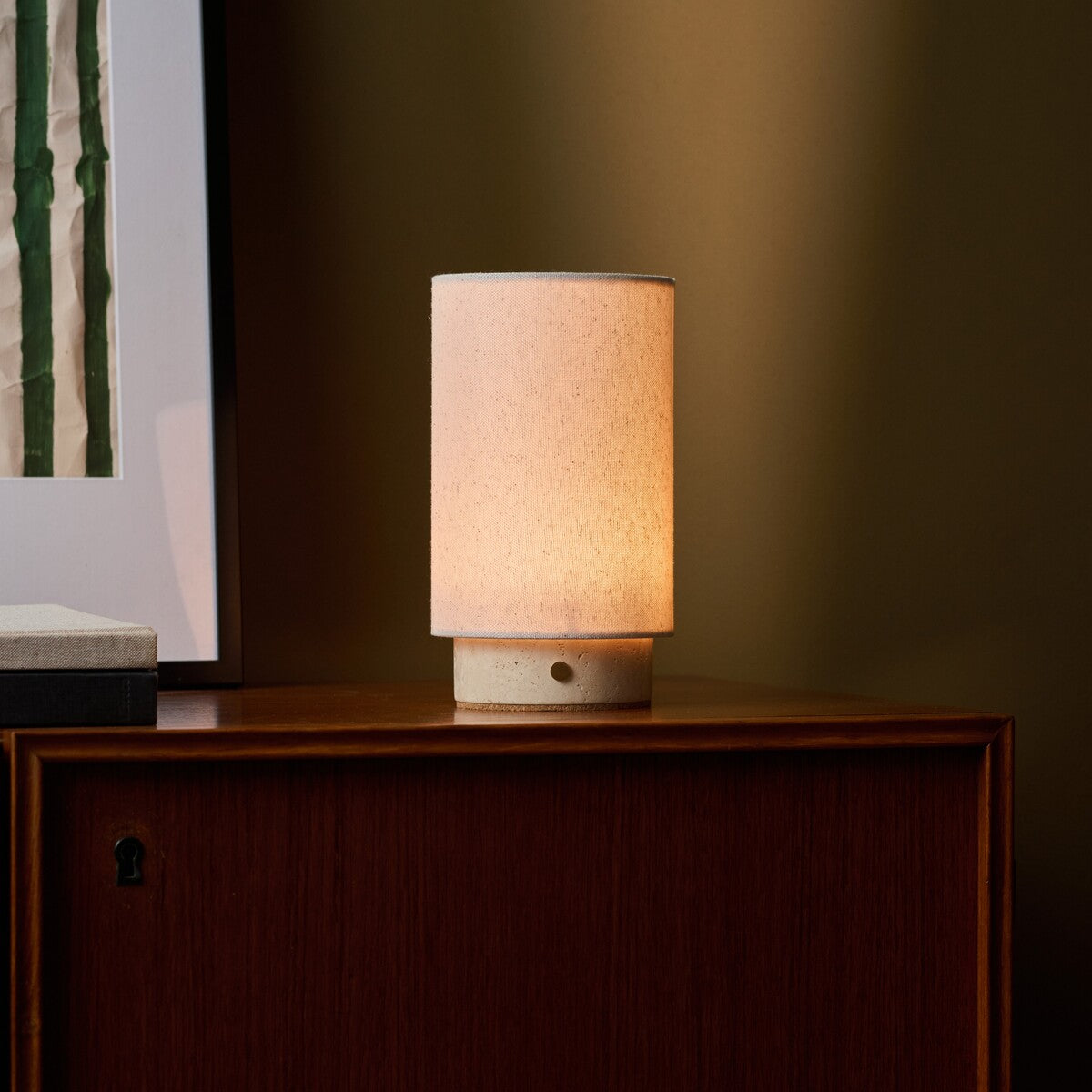 Floris cordless table lamp with travertine stone base on a wood sideboard beneath framed art