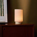 Floris cordless table lamp with travertine stone base on a wood sideboard beneath framed art