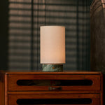 Floris cordless table lamp in Ice Green marble glowing on a bedroom dresser in front of striped blinds