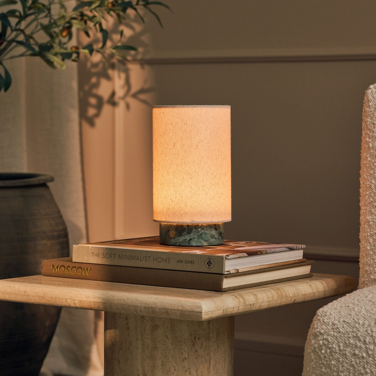 Tavellio Floris rechargeable table lamp in Ice Green marble glowing atop stacked books on a travertine side table