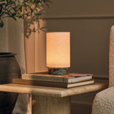 Tavellio Floris rechargeable table lamp in Ice Green marble glowing atop stacked books on a travertine side table