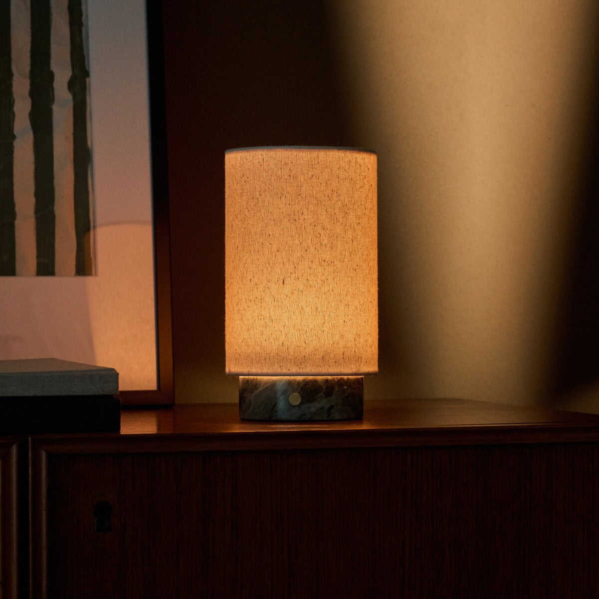 Tavellio Floris rechargeable table lamp in Ice Green marble glowing on a sideboard against a warm lit wall