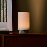 Floris cordless table lamp in Ice Green marble lit on a wooden sideboard beside a green striped art print