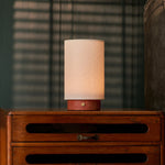 Floris cordless table lamp, red travertine base dimmed low on a nightstand with blinds casting shadows