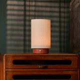 Floris cordless table lamp, red travertine base dimmed low on a nightstand with blinds casting shadows