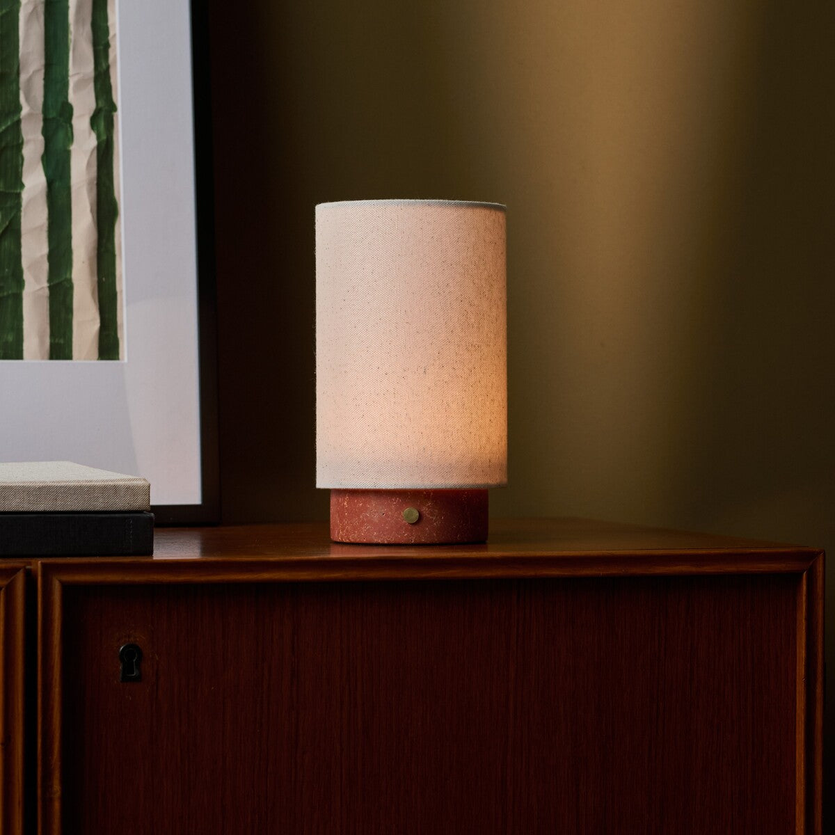 Floris rechargeable table lamp in red travertine beside a framed botanical print on a walnut sideboard