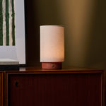 Floris rechargeable table lamp in red travertine beside a framed botanical print on a walnut sideboard