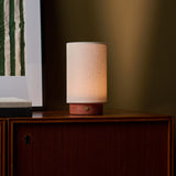 Floris rechargeable table lamp in red travertine beside a framed botanical print on a walnut sideboard
