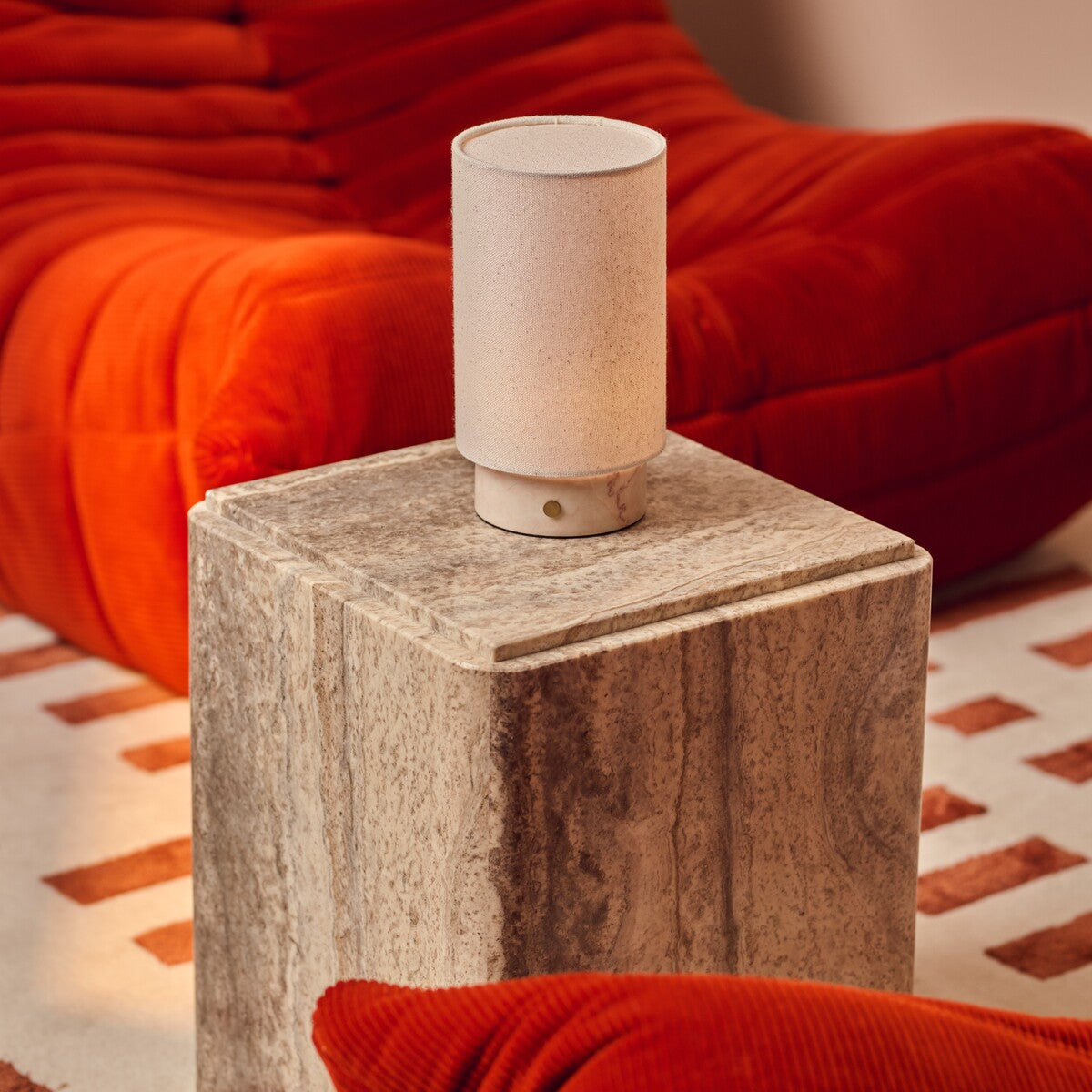 Tavellio Floris Rosa Aurora marble rechargeable table lamp on a travertine side table beside a bold orange sofa