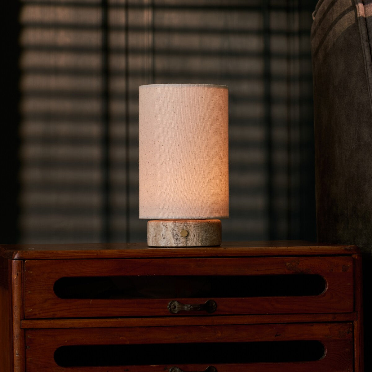 Floris Silver Travertine lampe de table sans fil Tavellio – sur une commode en bois près d'un store vénitien, silhouette éclairée le soir