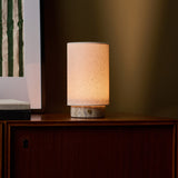 Floris Silver Travertine lampe de table rechargeable Tavellio – sur meuble bas devant un mur vert olive, veinures grises du socle visibles