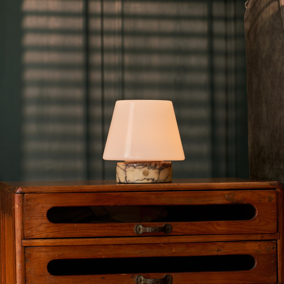 Tafellamp oplaadbaar Hooch Small in geel marmer, brandend op een vintage houten dressoir in de avond